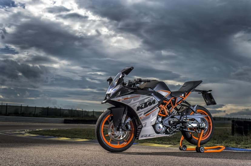 KTM RC 390 motorcycle with orange wheels on a race track under a dark, heavy grey cloudy sky.