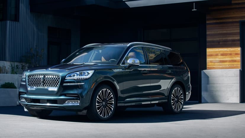 Dark teal Lincoln Aviator SUV parked in front of a modern house with wood siding and concrete walls.