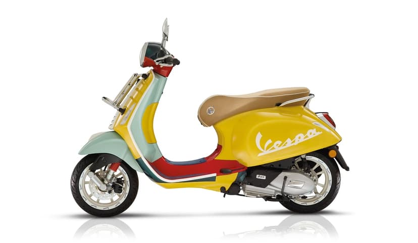 Multi-colored Vespa Primavera scooter with yellow body, mint green front, and red accents on a white studio background.