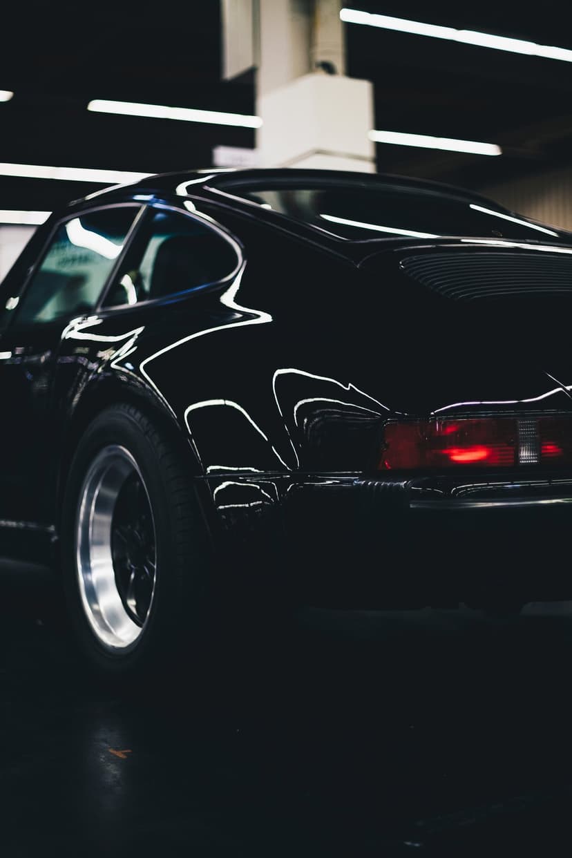 Black Porsche 911 rear showing a glowing red taillight bar, curved obsidian bodywork, and a silver alloy wheel.