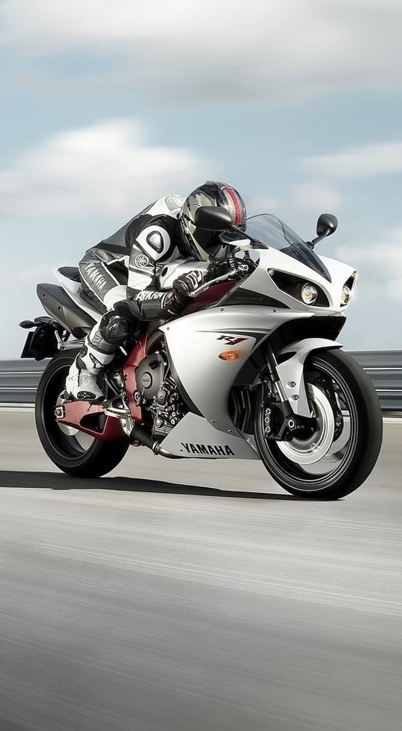 Racer on a white Yamaha R1 motorcycle leans into a track corner wearing professional gear and a full helmet.