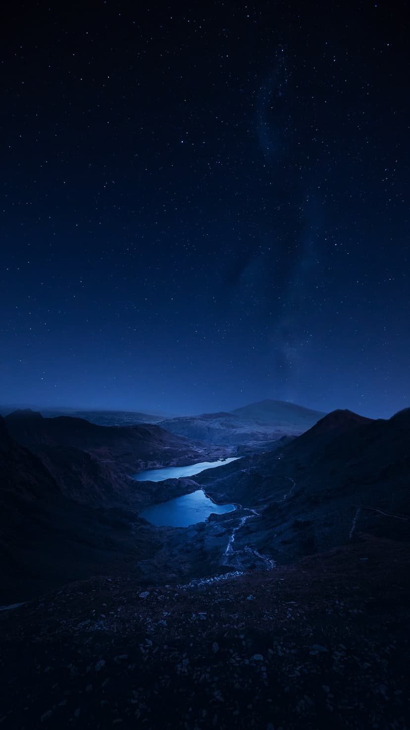 Milky Way galaxy and stars reflected in blue alpine lakes nestled between steep, dark mountain silhouettes.