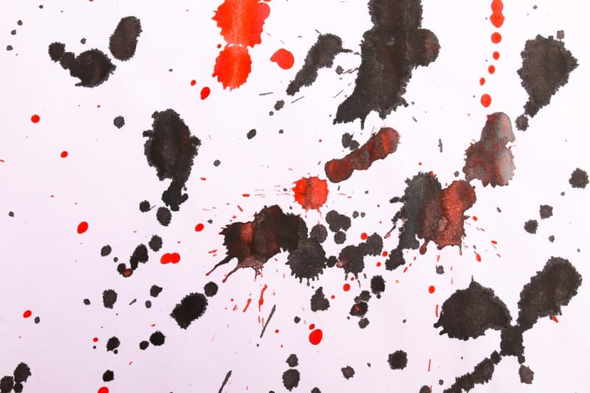 Black and red ink splashes scatter across a plain white surface with detailed droplets and organic textures.