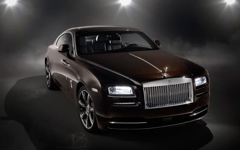 Rolls-Royce Wraith coupe in dark bronze metallic paint with glowing headlights in a smoky studio environment.
