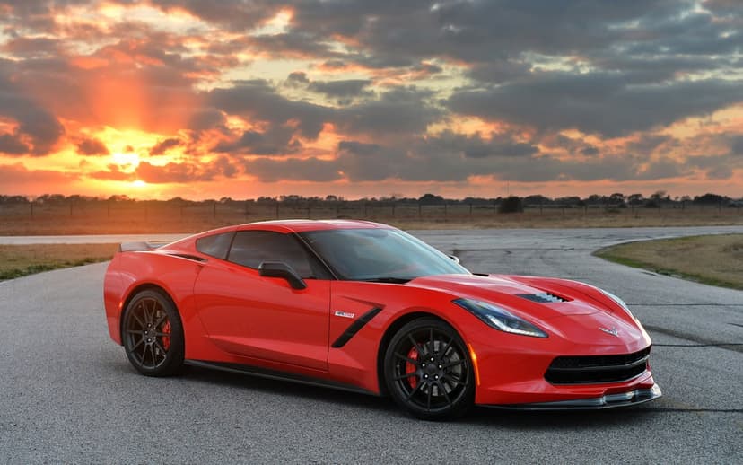 Red Chevrolet Corvette C7 on a racetrack against a dramatic orange and cloudy sunset sky during golden hour.