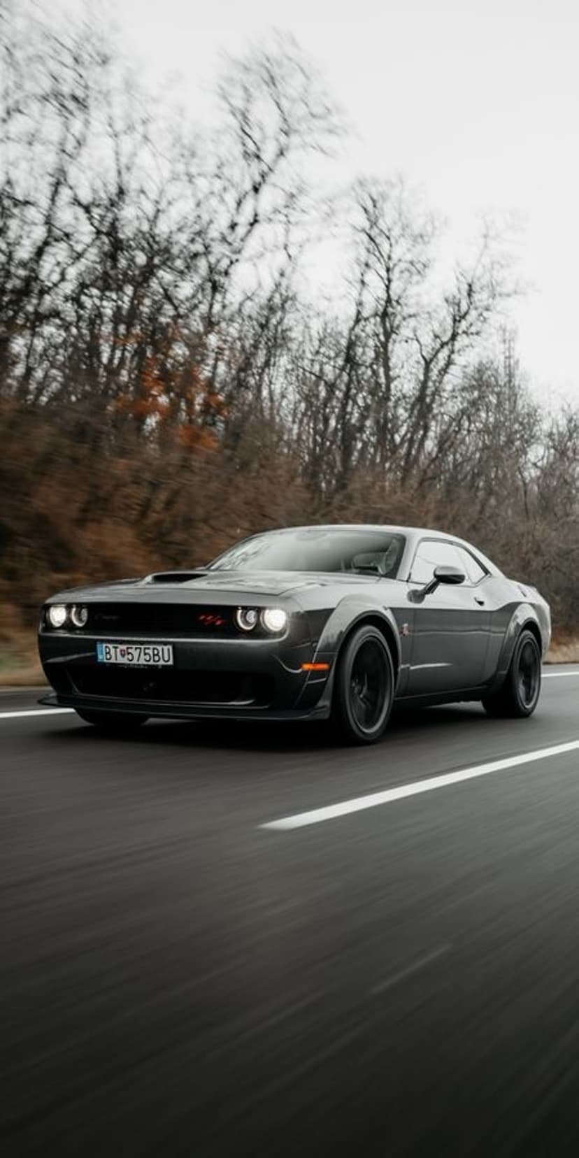 Dark gray Dodge Challenger SRT Hellcat Widebody drives on a road under a moody, overcast winter sky.