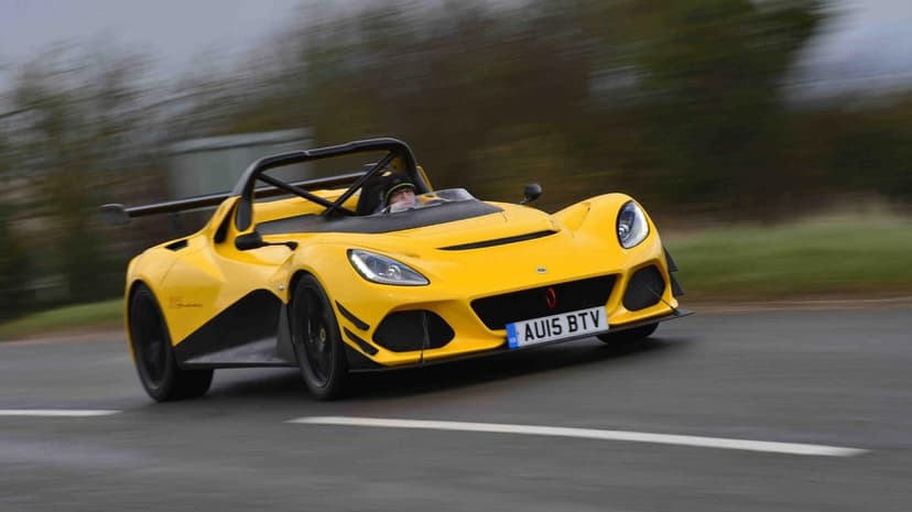 Yellow open-top Lotus 3-Eleven sports car racing on a road with motion blur background and driver visible.