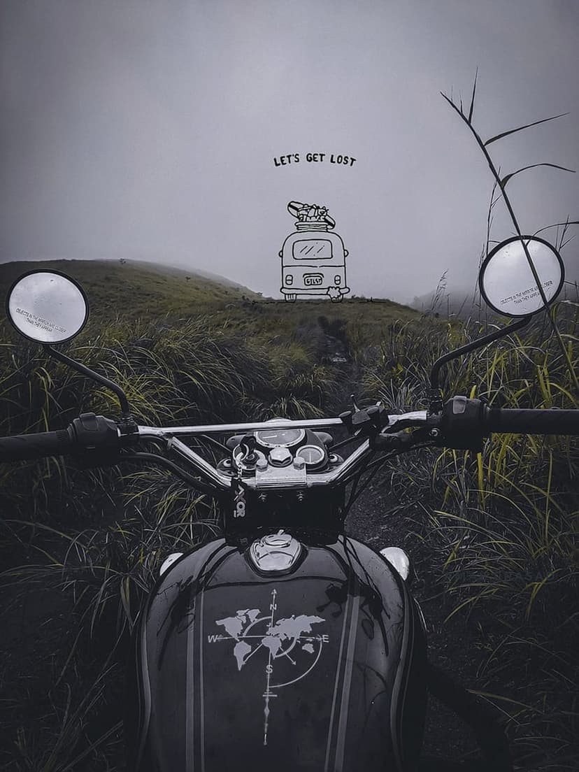 Adventure motorcycle parked on a green ridge with a world map on its gas tank under a misty mountain sky.