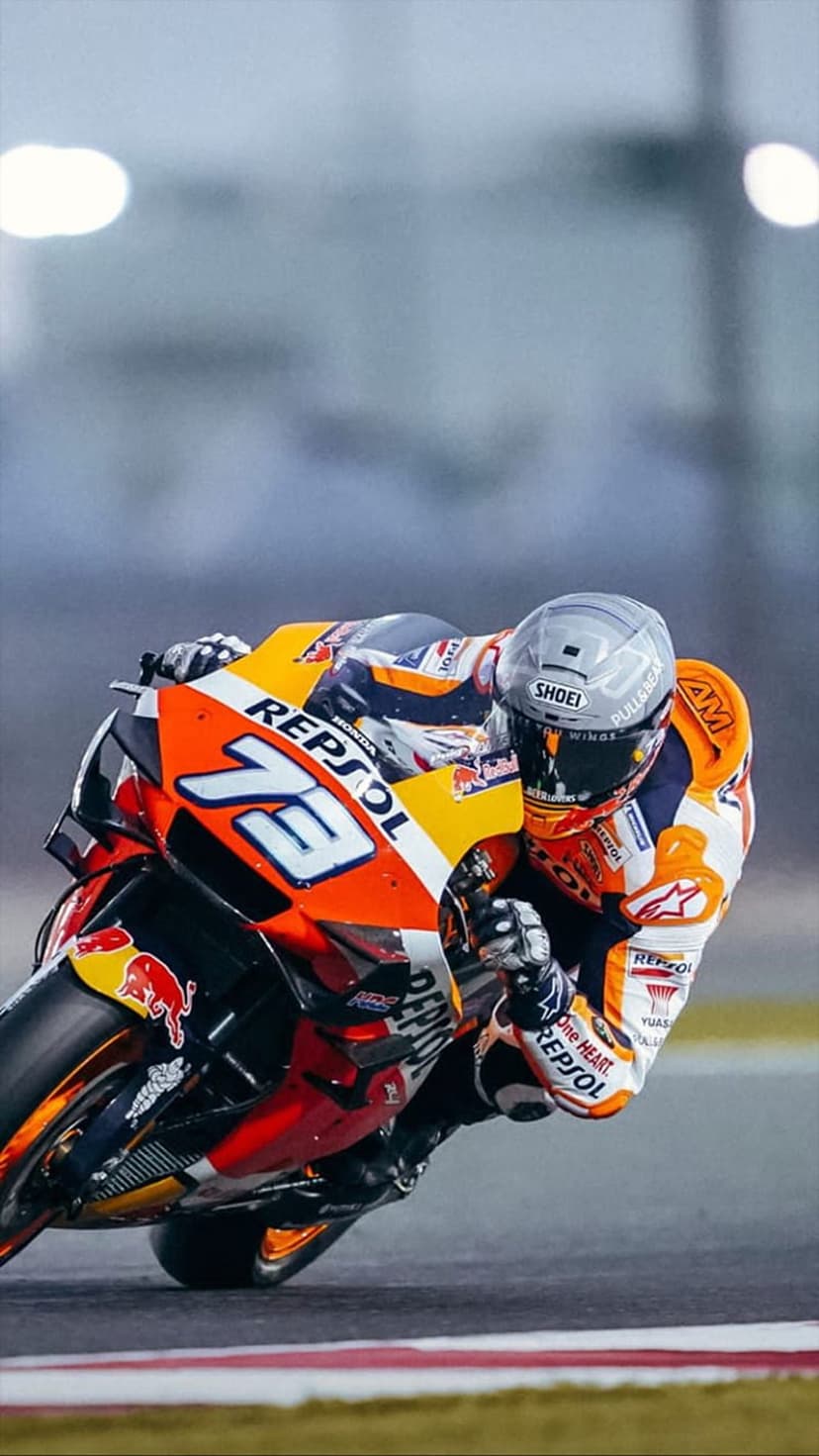 MotoGP rider Joan Mir leans into a racetrack corner on a colorful Repsol Honda motorcycle at high speed.