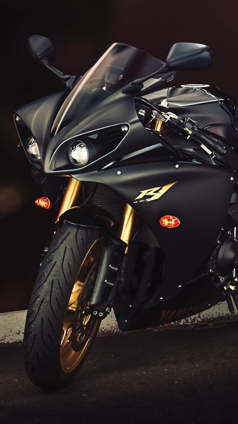 Yamaha R1 sportbike front view featuring matte black bodywork, golden forks, and dual headlights on a dark background.
