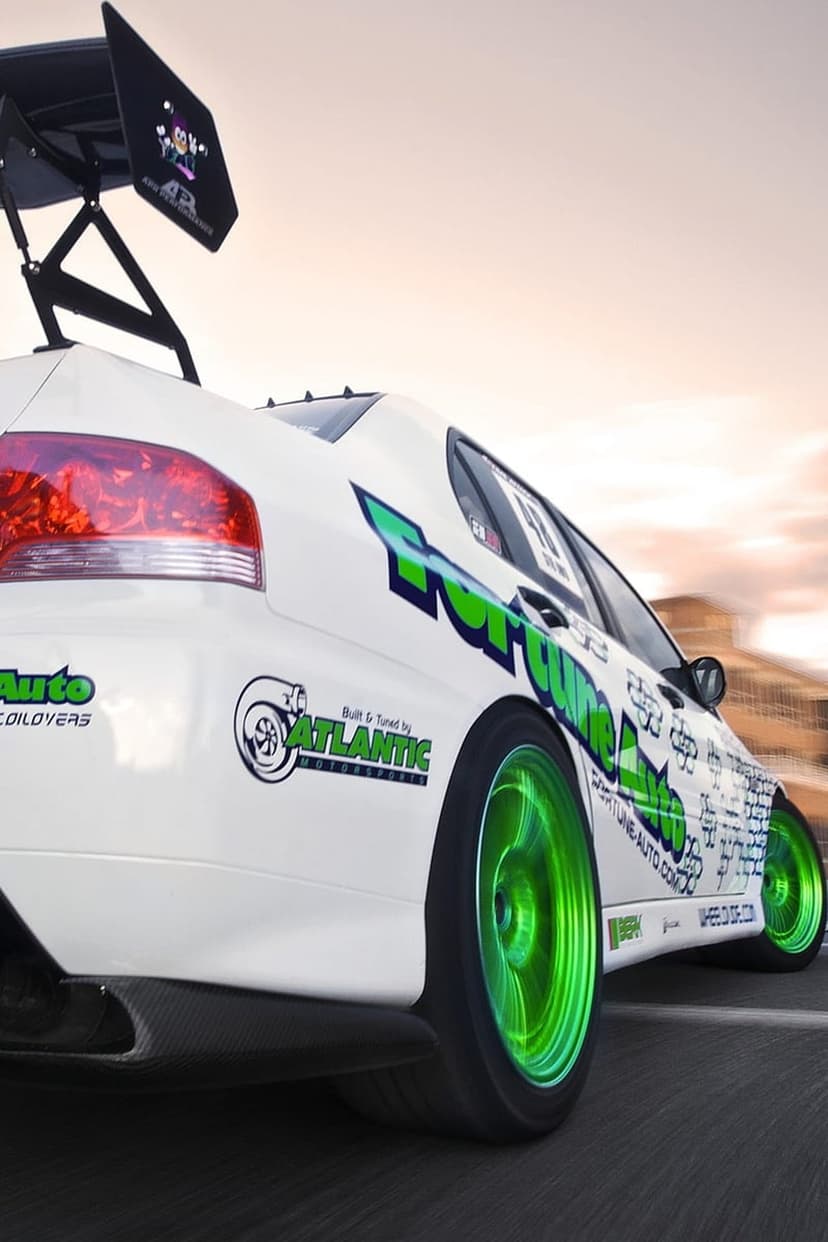White Mitsubishi Lancer Evolution with a large rear wing and neon green wheels driving fast on a paved road.
