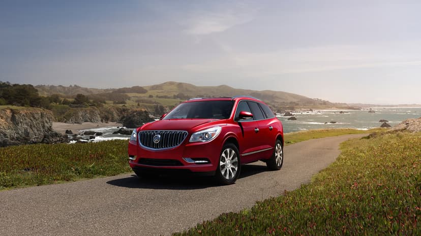 Red Buick Enclave SUV parked on a coastal road overlooking rocky cliffs and the blue ocean under a clear sky.