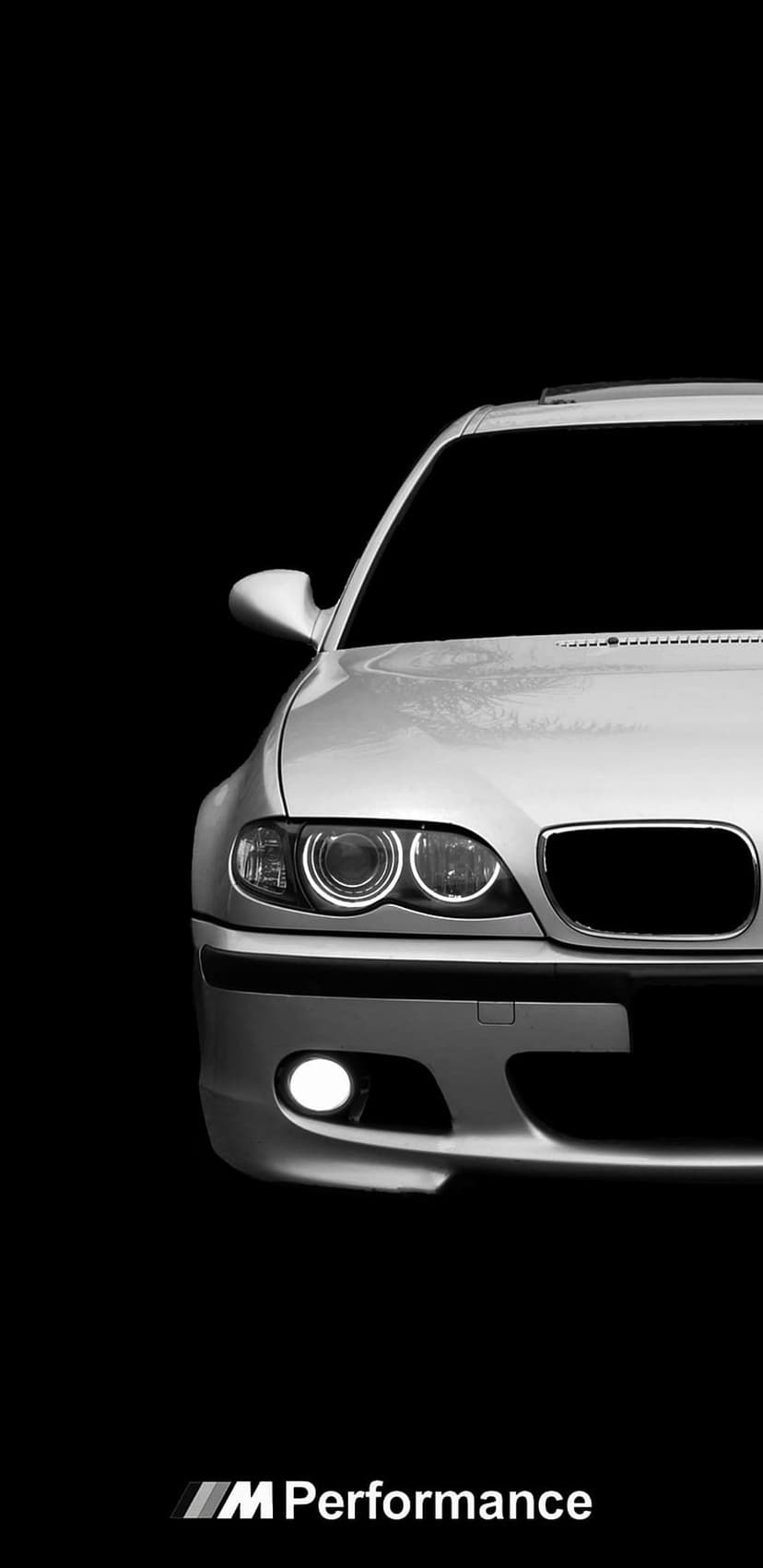 BMW M Series front grille and glowing LED headlights centered against a pitch black background in monochrome.