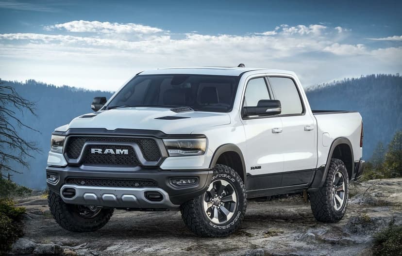 White Ram 1500 Rebel truck with off-road tires parked on a rocky cliff under a blue sky with mountain views.