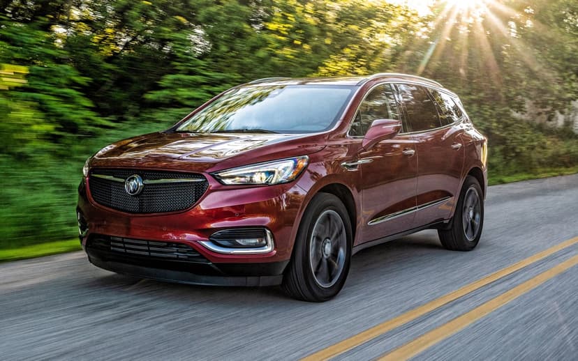 Maroon Buick Enclave SUV driving on a tree-lined road with golden sunlight filtering through leaves.