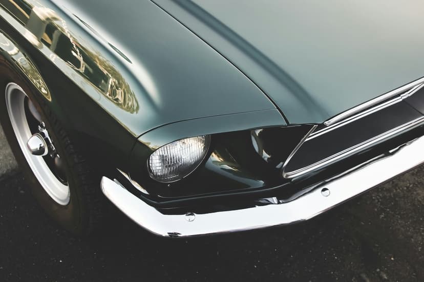 Dark green vintage car front with a round glass headlight, chrome bumper, and metallic grille textures.