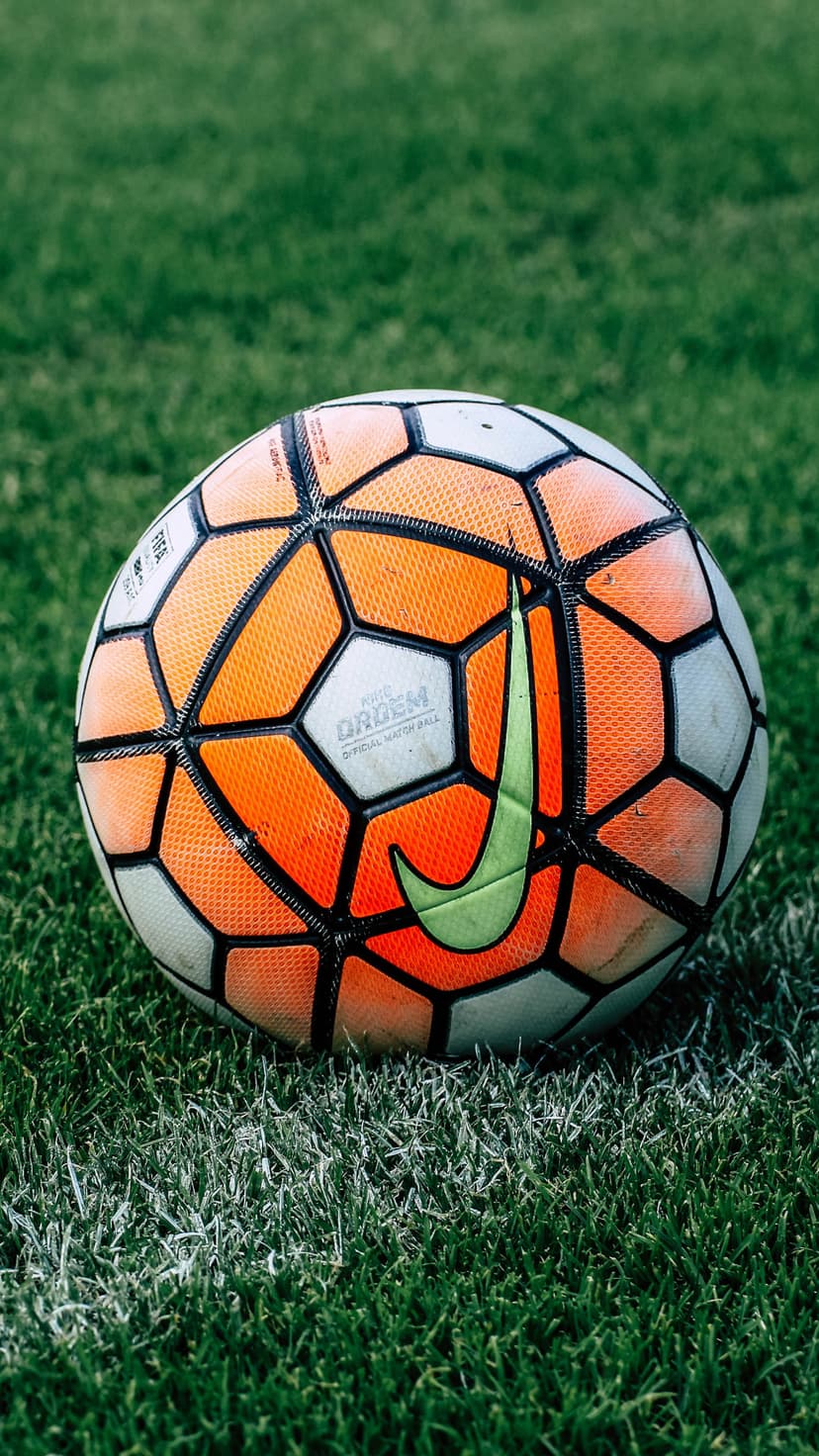 Orange and white Nike soccer ball with a green swoosh logo resting on a textured grass field with white paint lines.
