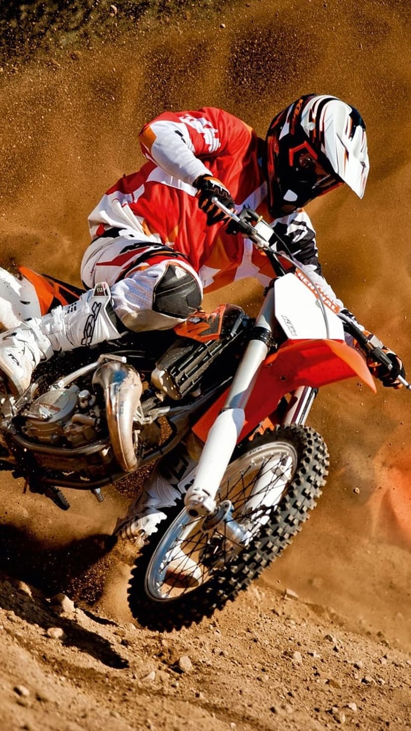 Motocross rider in red and white gear leaning into a sharp dirt turn with earth spraying from the tires.