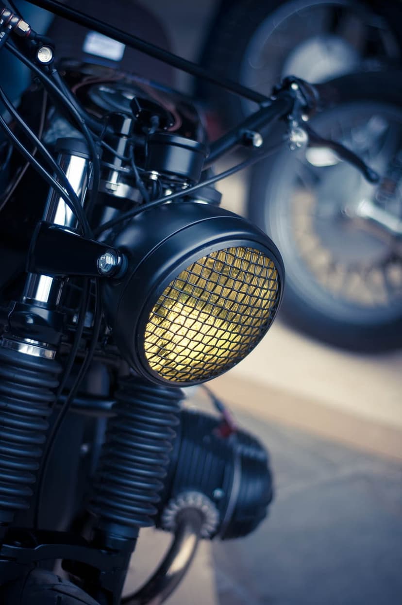 Vintage black motorcycle headlight with a yellow mesh grille, exposed suspension springs, and handlebars.