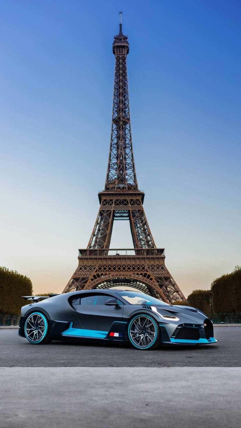 Matte gray Bugatti Divo supercar with cyan wheels parked in front of the Eiffel Tower in Paris at dusk.