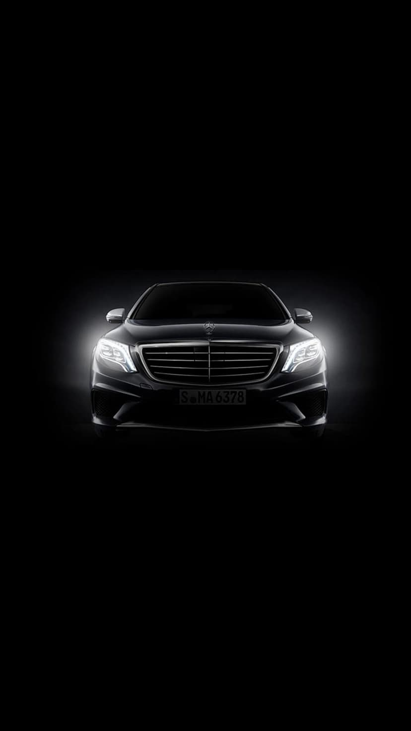 Mercedes-Benz S-Class LED headlights and chrome grille glowing against a pitch-black background at night.