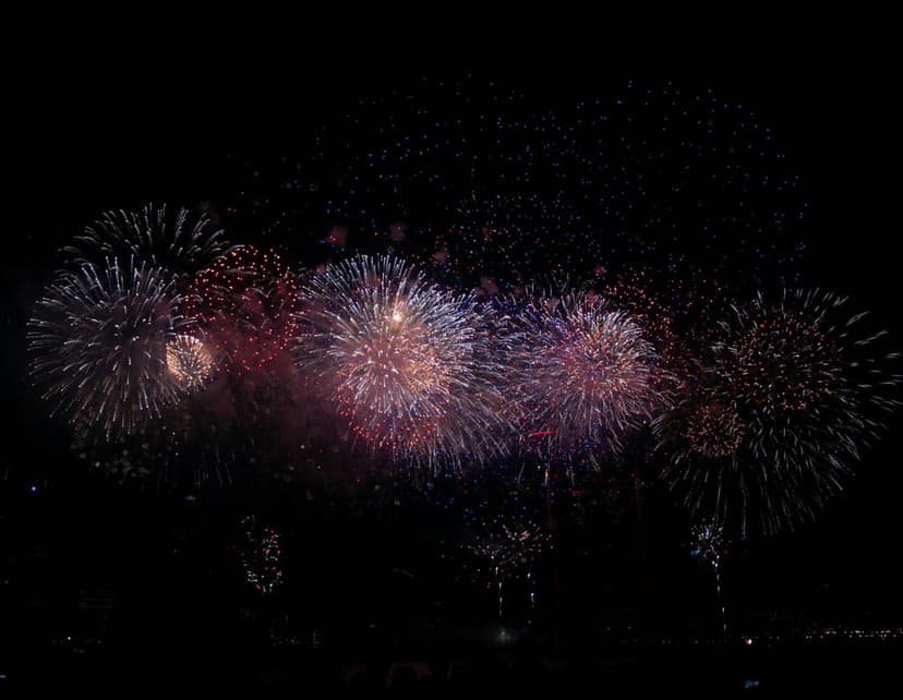 Crimson and blue fireworks exploding with shimmering light trails against a dark night sky in vertical orientation.