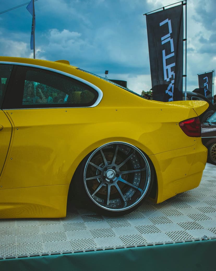Yellow custom sports car with lowered suspension and wide aftermarket wheels at an outdoor automotive event.