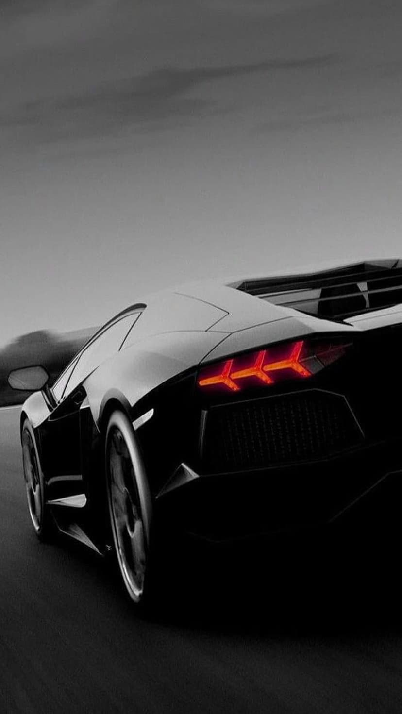 Lamborghini Aventador tail lights glow red against a black car body and a blurred grayscale road background.