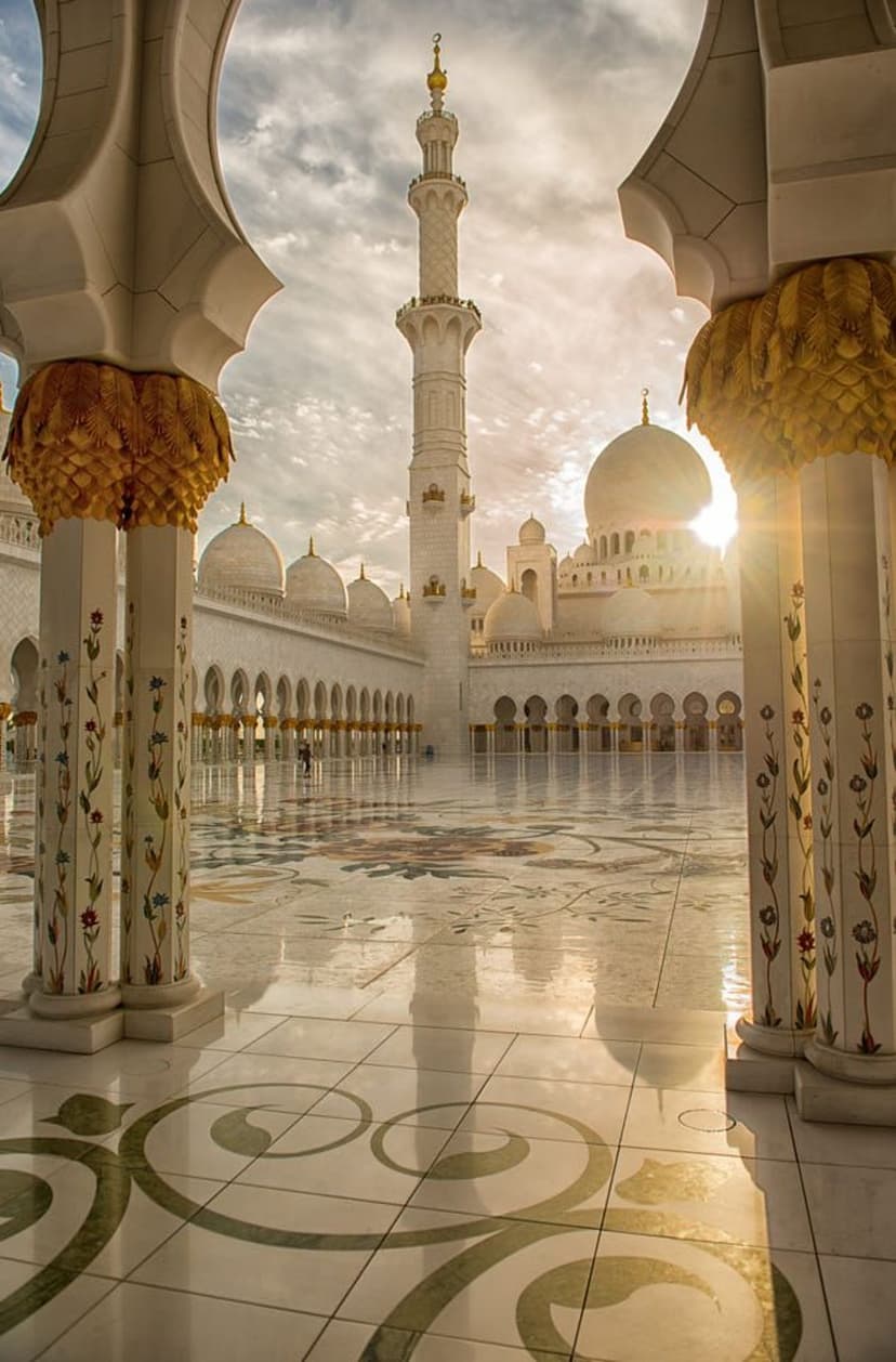 White marble courtyard of the Sheikh Zayed Grand Mosque at dawn with floral floor patterns and tall minarets.