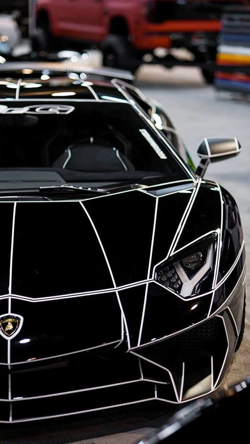 Black Lamborghini sports car with white geometric stripes and LED headlights angled for a vertical phone screen.
