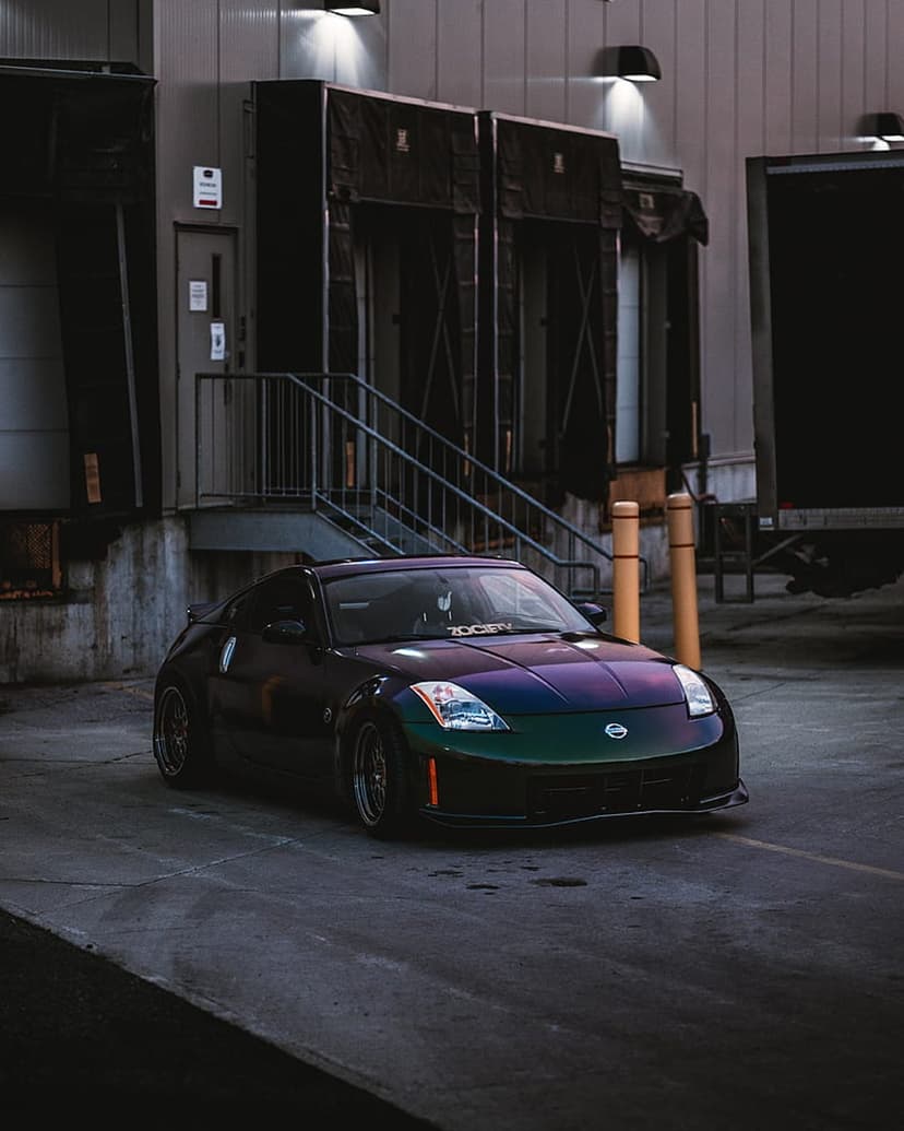 Nissan 350Z with iridescent purple-green paint parked by a concrete loading dock at dusk under soft twilight sky