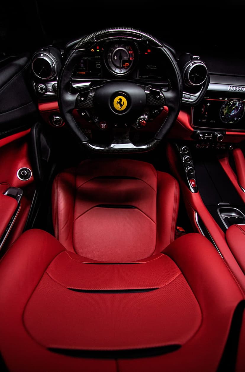 Ferrari steering wheel with logo and red leather seats inside a high-performance Italian supercar cabin.