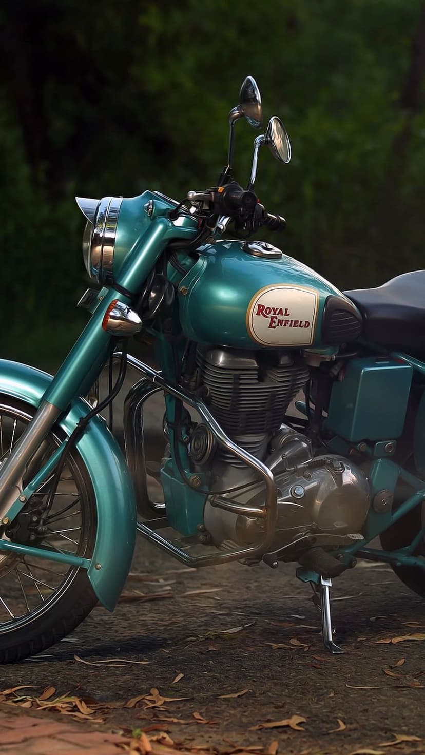 Teal Royal Enfield motorcycle showing a chrome engine and fuel tank logo on a path with scattered brown leaves.