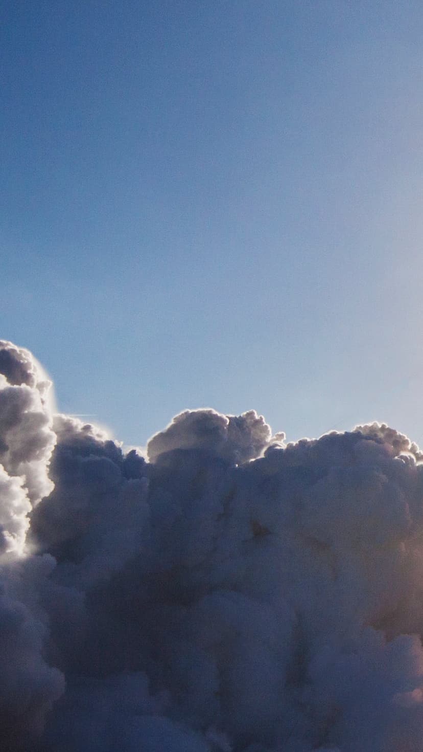 Dark billowing clouds with bright sunlit silver linings against a clear blue sky in a vertical composition.