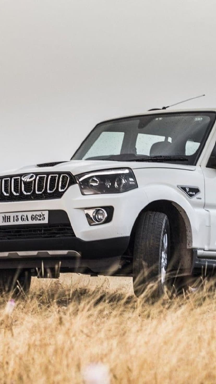 White Mahindra Scorpio SUV parked in a field of dry golden grass under a cloudy overcast sky during daytime.