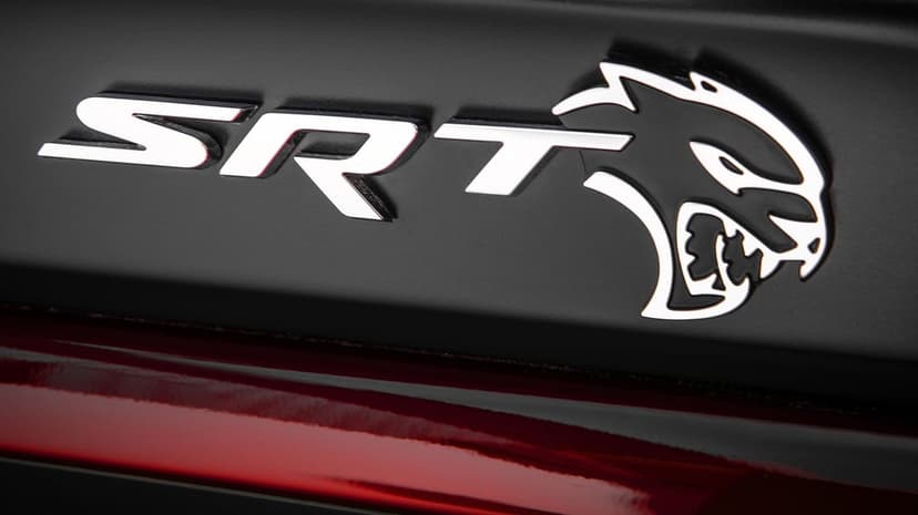 Polished chrome SRT Hellcat emblem on a matte black surface above a glossy deep red metallic car body panel.