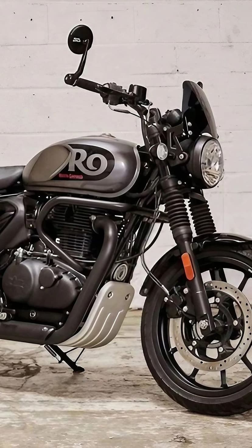 Royal Enfield Hunter 350 motorcycle with a round headlight and chrome engine against a white brick wall.