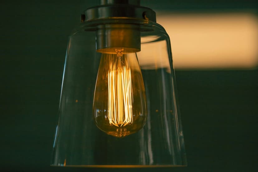 Edison light bulb with a glowing orange filament inside a clear glass pendant lamp casting warm amber light.