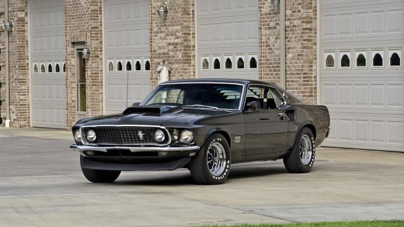 Black 1969 Ford Mustang Boss 429 parked in front of brick garage doors under natural daylight.