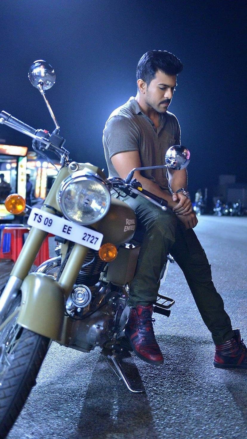 Man with a mustache sits on a vintage motorcycle wearing red sneakers and green pants in a dark urban setting.