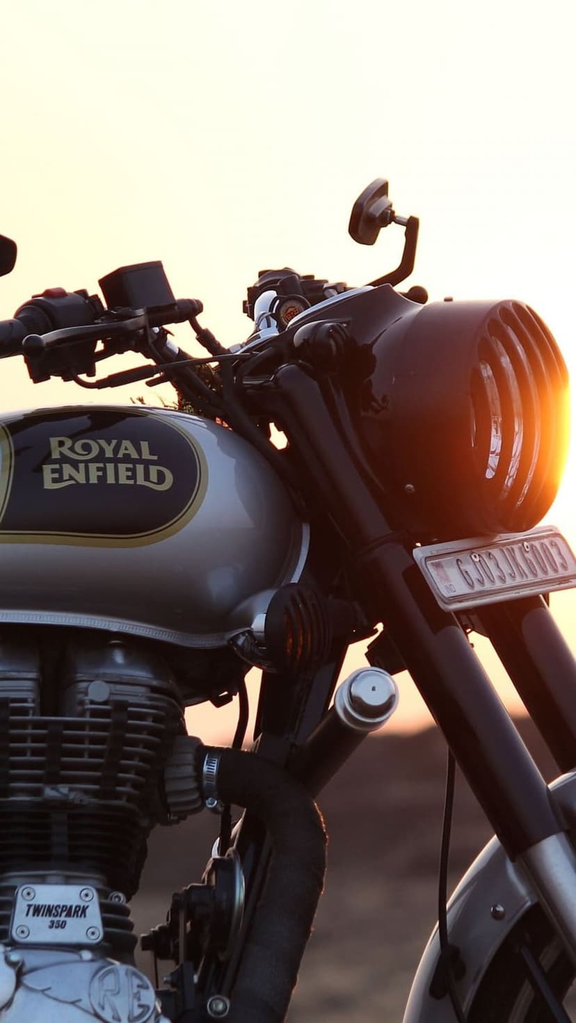 Royal Enfield fuel tank and engine glisten under a warm orange sunset in a detailed vertical close-up shot.