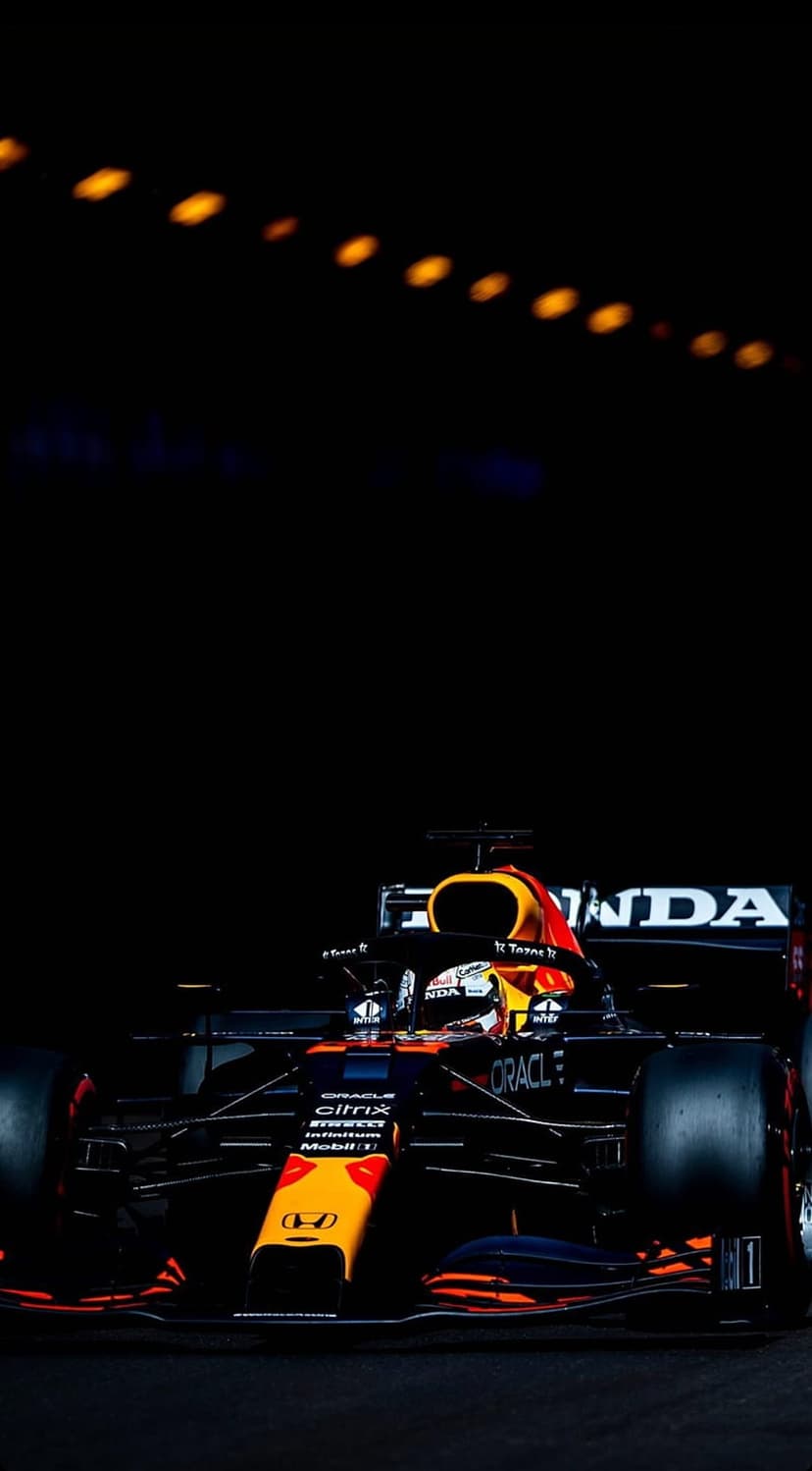 Max Verstappen's Red Bull F1 car featuring orange and navy livery glows under bright night track floodlights.