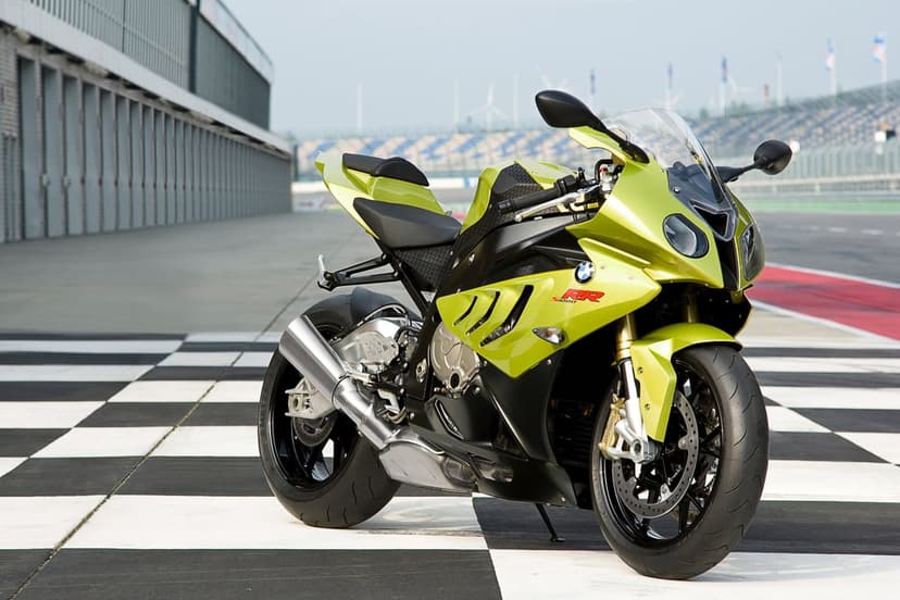 Acid green BMW S1000RR sportbike parked on a checkered race track grid with pit garages in the background.