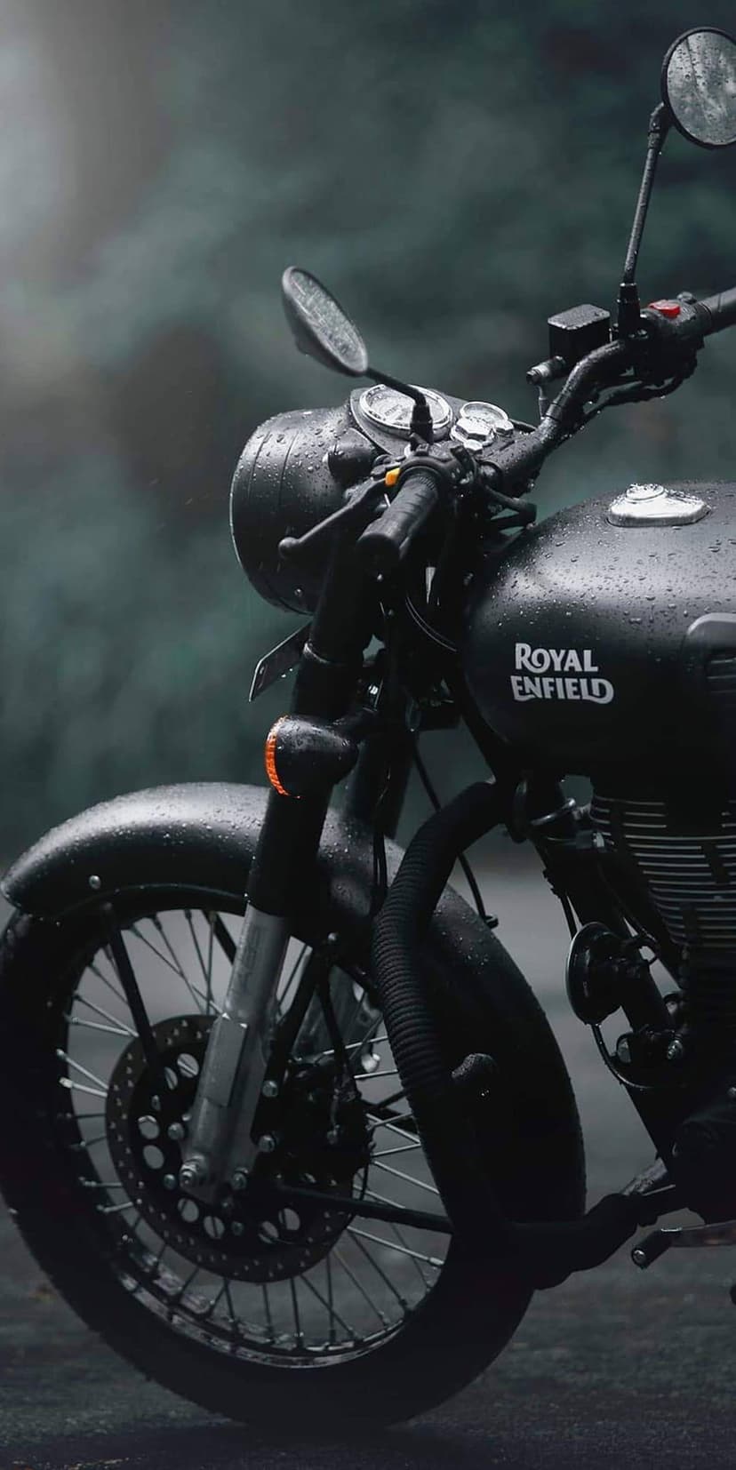 Royal Enfield motorcycle covered in raindrops stands parked in a thick gray fog with wet metallic details.