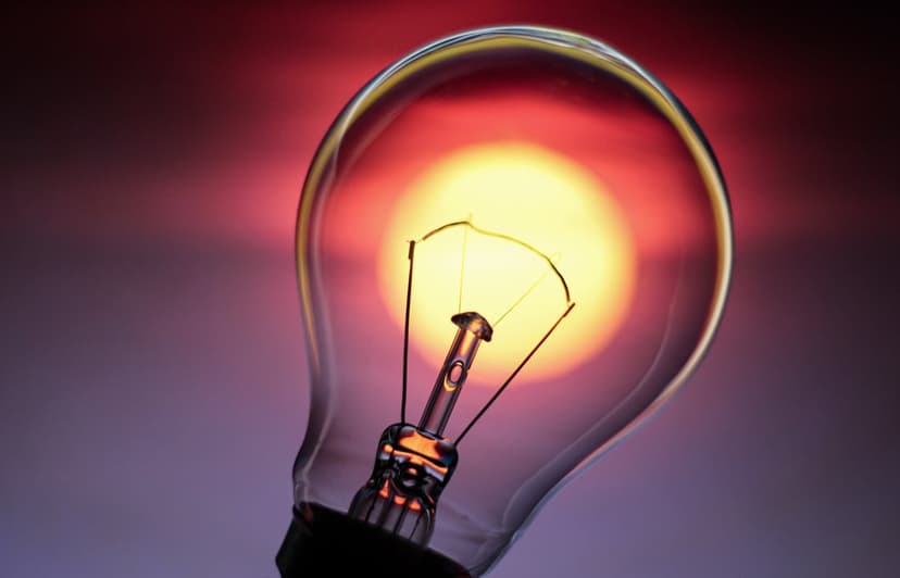 Incandescent bulb filament glows brilliantly with yellow light against a red and purple gradient background.