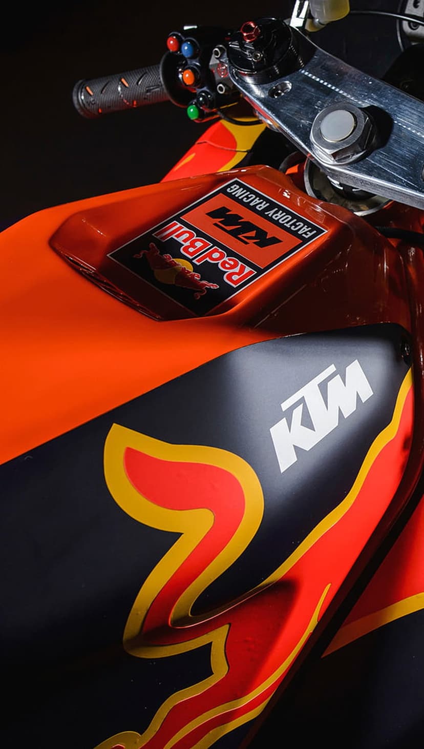 KTM racing motorcycle close-up featuring orange fairings, Red Bull branding, and intricate handlebar mechanics.