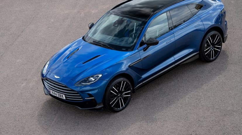 Blue Aston Martin DBX luxury SUV viewed from above on an asphalt road with multi-spoke wheels and black roof.