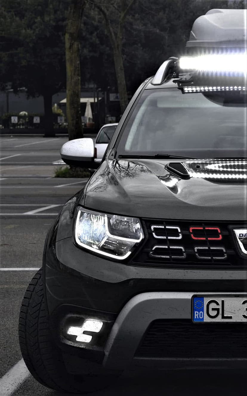 Dacia Duster SUV with an illuminated roof LED light bar, glowing fog lamps, and red grille accents at night.
