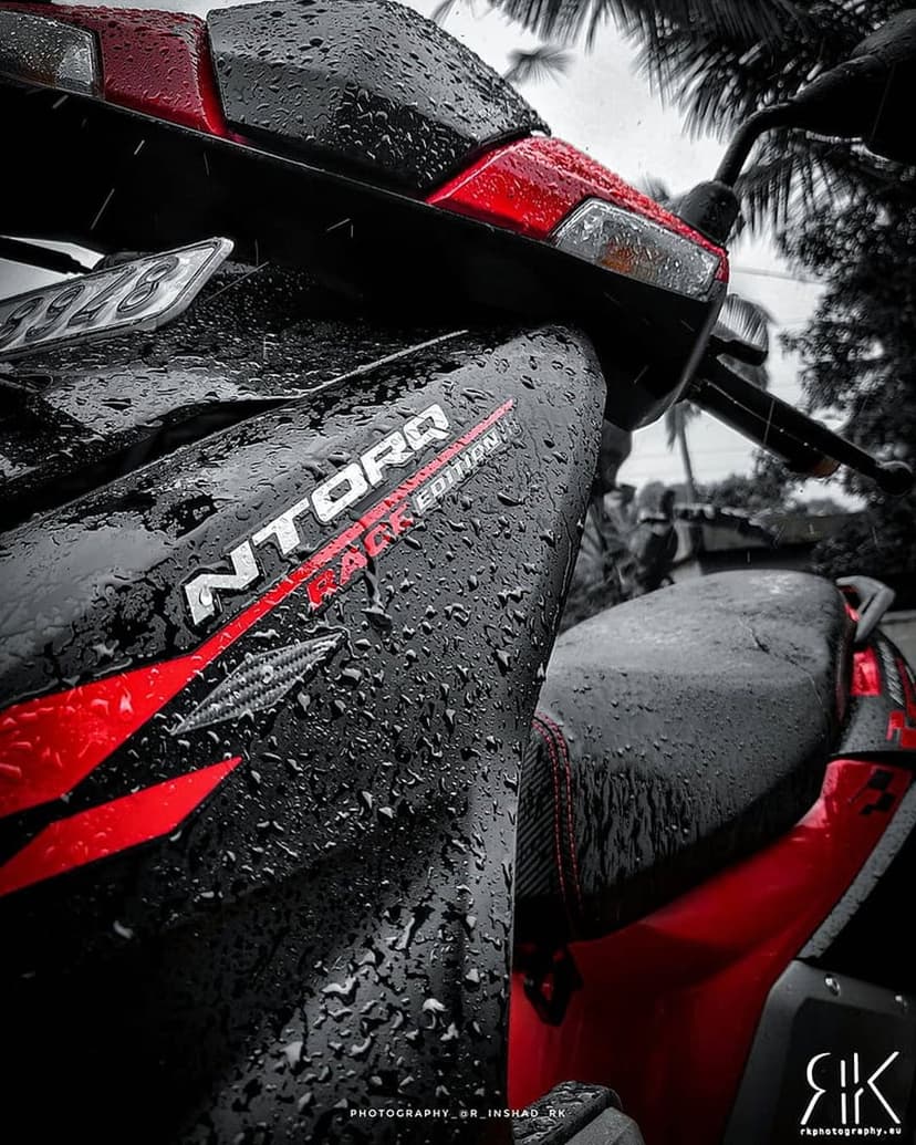 Red and black sport scooter with rain droplets on its body panels and NTORQ logo in a close-up macro shot.