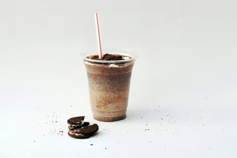 Oreo milkshake in a clear cup with a red straw and cookie crumbs on a white surface for a phone backdrop.